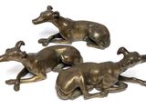 three bronze sculptures of greyhounds laying down on a white surface
