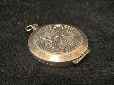 une vieille montre de poche en argent ornée d'une croix, posée sur un tissu noir