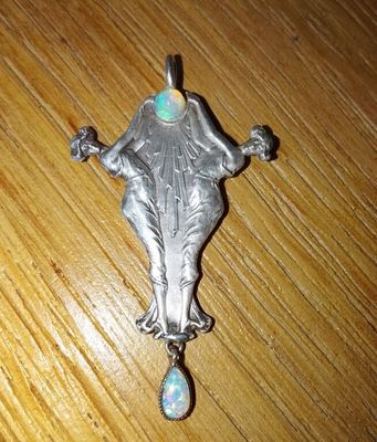 croix en argent avec un pendentif en forme d'oplite, posée sur une table en bois, sur une surface en bois