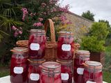 several jars of jam sit on a table in front of a basket of flowers