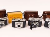 several old cameras are lined up in a row on a white surface