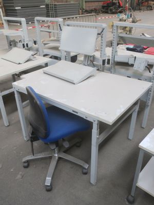 de nombreux bureaux et chaises dans un entrepôt, avec un ordinateur posé dessus