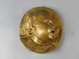 plaque en laiton représentant le visage d'un bébé sur fond blanc