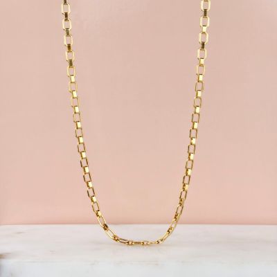un collier à chaîne en or avec des maillons carrés sur fond rose