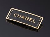 une broche noire et dorée sur laquelle est inscrit le mot « Chanel »