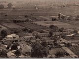 une vieille photo représentant une ferme et des terres agricoles, survolées par un avion