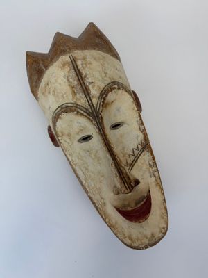 un vieux masque en bois accroché à un mur sur fond blanc