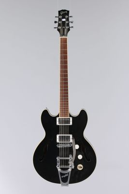 une guitare électrique noire posée sur une surface blanche