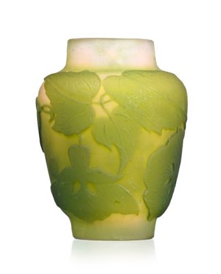 a green vase with leaves on it on a white surface