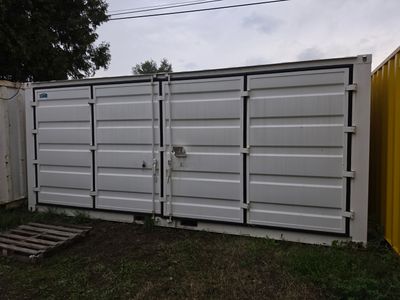 un conteneur blanc posé dans une cour, à côté d'une clôture jaune
