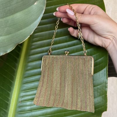 a woman holding a gold purse with a chain hanging from it