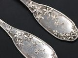 two silver spoons with floral designs on them on a black surface