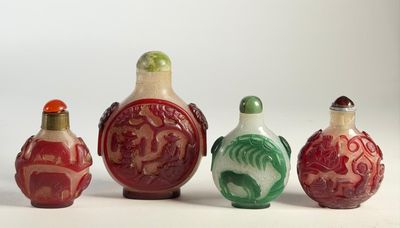 Quatre petites flacons à tabac chinois en verre sont alignés sur une surface blanche