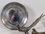 a silver plate with a bird and a bird figurine next to it