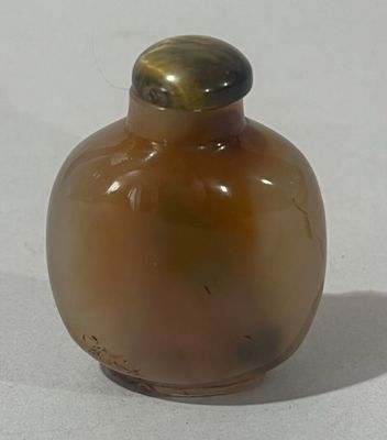 une petite bouteille en verre avec un bouchon doré, posée sur une surface blanche