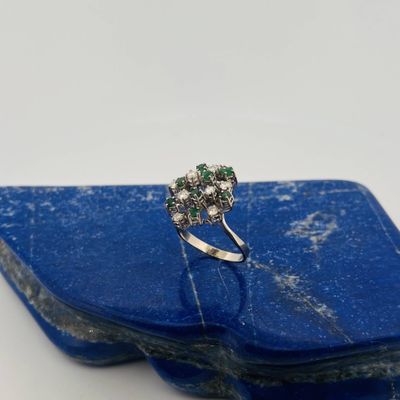 a close up of a diamond and emerald ring on a blue stone