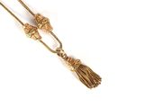 a close up of a gold necklace with a tassel on a white background