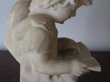 marble statue of a boy reading a book on a wooden table