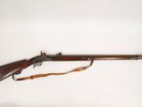 Un vieux fusil est posé sur une surface blanche, tandis qu'un homme l'observe