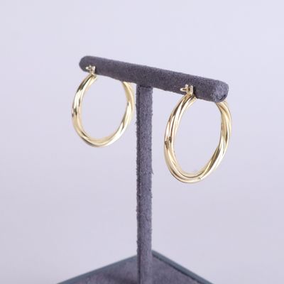 un gros plan sur une paire de boucles d'oreilles créoles en or posées sur un présentoir