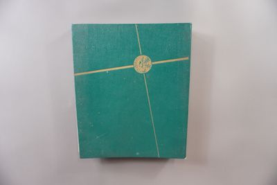 un vieux livre vert avec une bordure dorée sur une couverture blanche