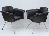 pair of black leather chairs with chrome legs against a white wall