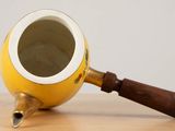 a yellow tea pot with a wooden handle sitting on a table