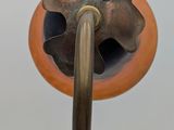 an orange vase with a metal handle on a stand
