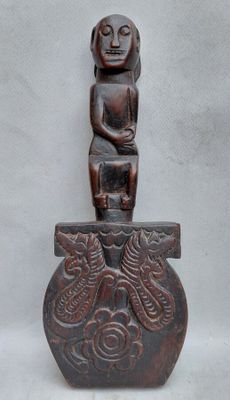 une statue en bois représentant une personne assise sur un vase