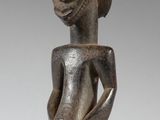 une statue en bois représentant une femme, dont la tête repose sur un socle