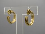 paire de boucles d'oreilles créoles dorées présentées sur un support en acrylique transparent
