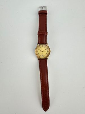 gros plan d'une montre sur une surface blanche avec un bracelet marron