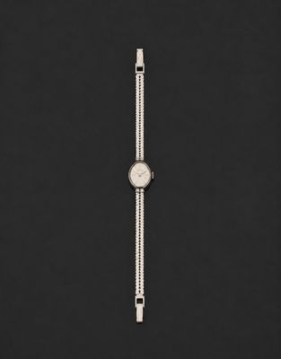 une montre argentée posée sur une surface noire avec un fond noir