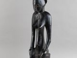 une photo représentant la statue d'un homme assis sur un tabouret