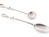 une paire de cuillères en argent posées sur une surface blanche, sur fond blanc