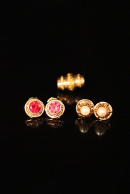 three pairs of gold earrings with pink stones on a black surface