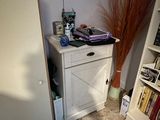 a white cabinet in the corner of a room with a vase and bookshelf