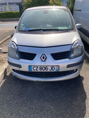 La voiture argentée est garée sur le parking, à côté de la camionnette blanche.