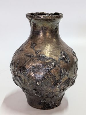 a silver vase that is sitting on a white surface