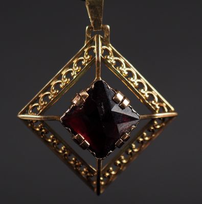 a close up of a gold pendant with a red stone in it