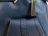 blue leather handbag on a wooden table with a tag attached to it