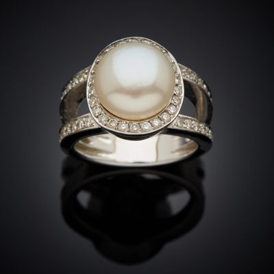a white pearl and diamond ring on a black surface