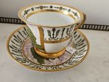 une tasse à thé et sa soucoupe ornées d'une bordure dorée, posées sur une table en marbre