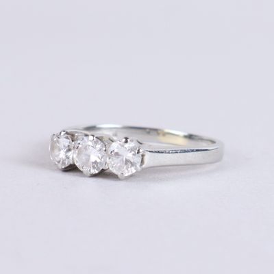 un gros plan d'une bague en diamant à trois pierres posée sur une surface blanche