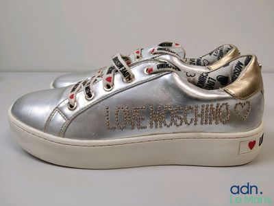 Des baskets argentées ornées de cœurs rouges sont posées sur une surface blanche