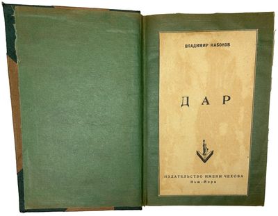 an old book with a green cover sitting open on a white surface
