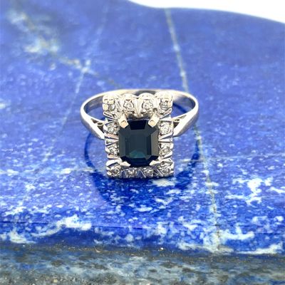 une photo d'une bague sertie d'un saphir bleu et de diamants, posée sur une pierre bleue
