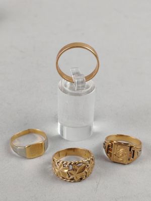 three gold rings and a glass container on a white surface