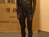 une statue en bronze représentant un homme debout à côté d'un panneau