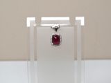 une photo d'un pendentif composé d'une pierre rouge et d'un diamant, présenté dans une vitrine transparente